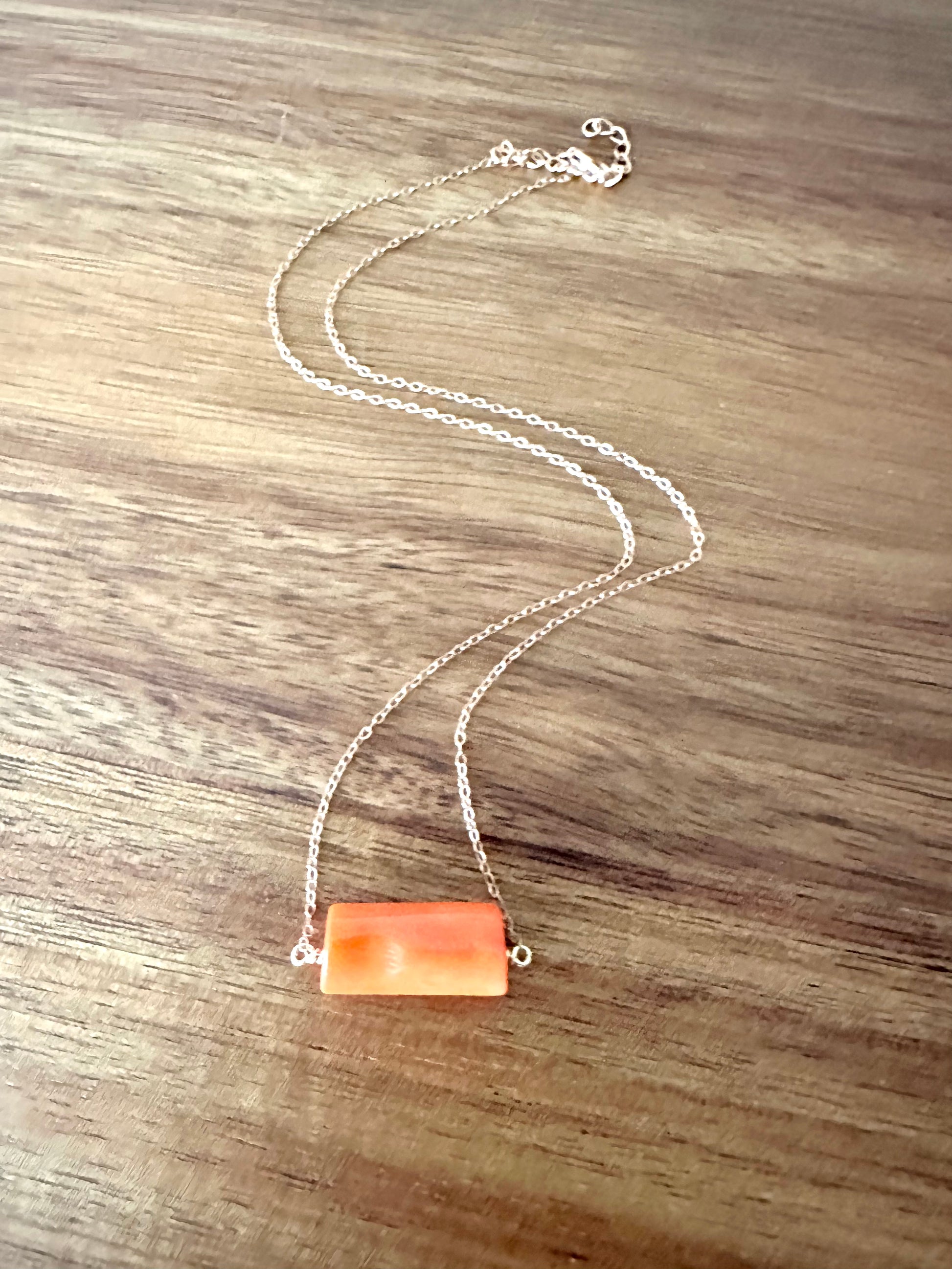 an orange bar of coral wirewrapped on a rosegold chain ona wooden background