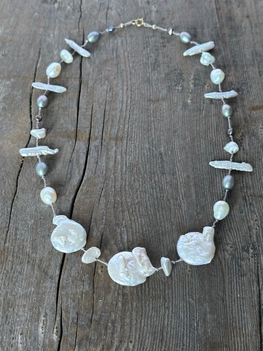 a necklace with three large cloud shaped white pearls and smaller white and grey perals on a wooden background.