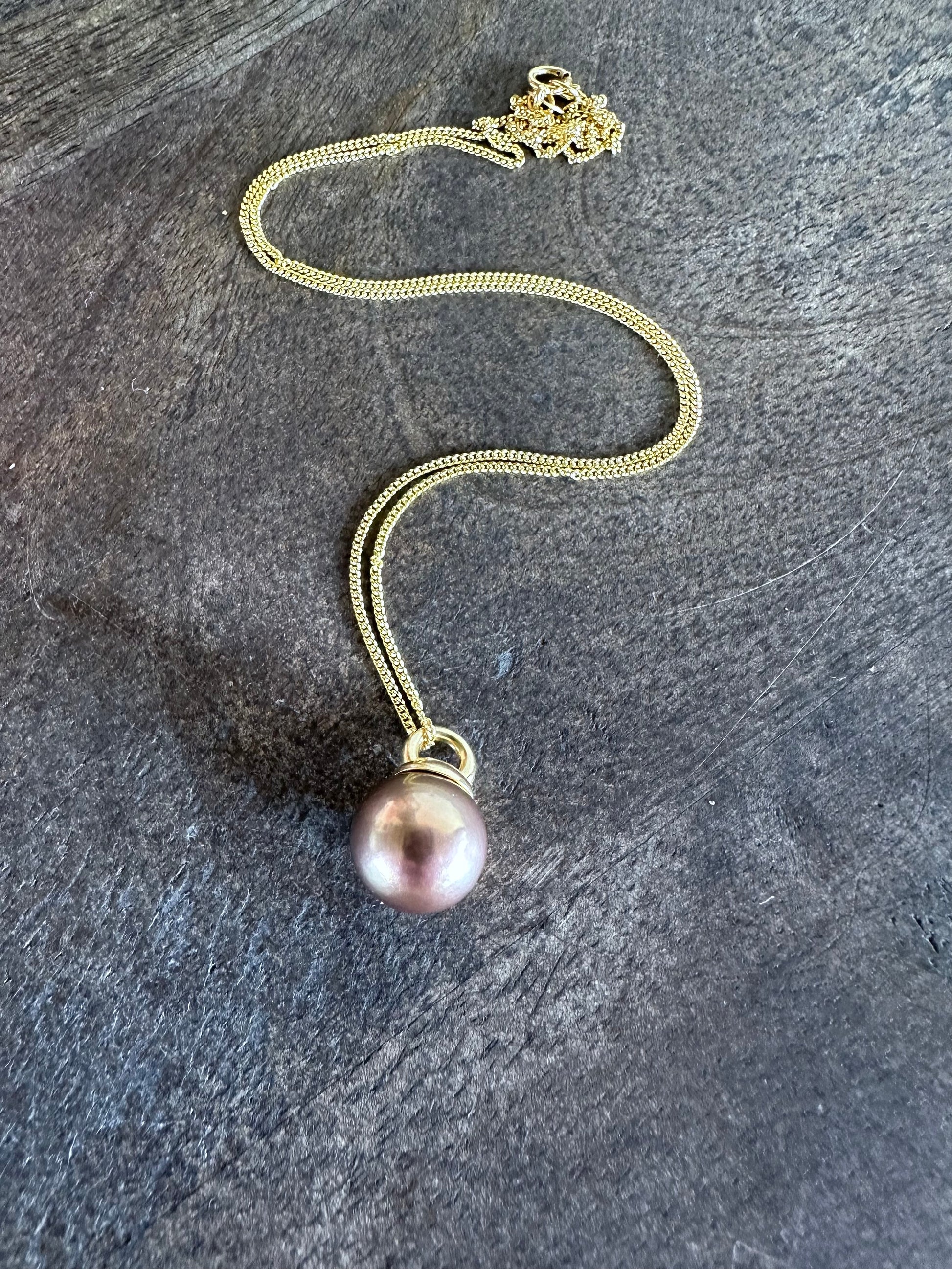 a copery pink round pearl necklace on a gold chain is on a grey wooden background