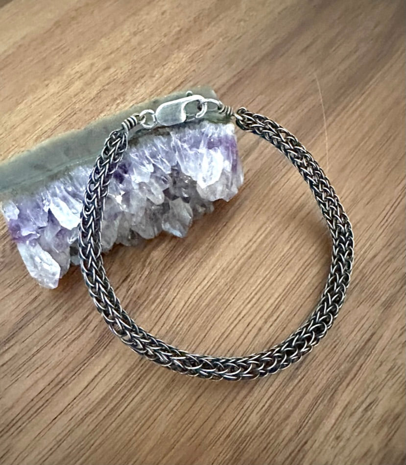 a silver knit bracelet on a wooden background with an amethyst stone as a prop