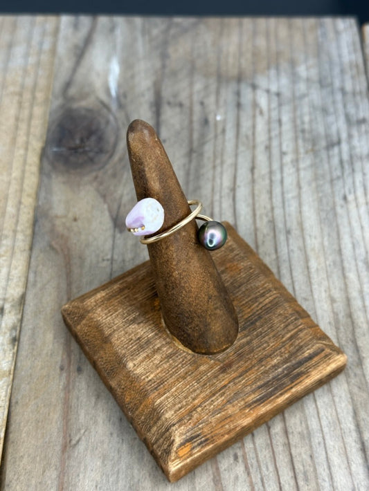 a ring on a wooden ring stand with a purple shell and a tahitian pearl on a wire that twists