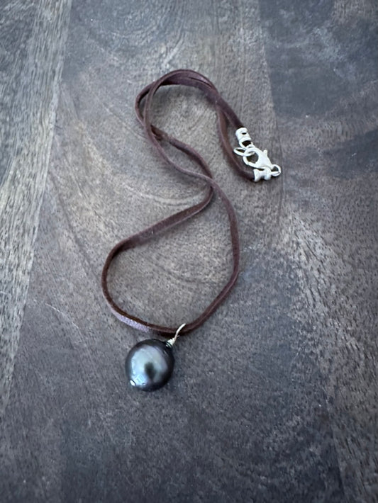a leather necklace with a tahitain balck pearl on it and silver clasp on a wooden background
