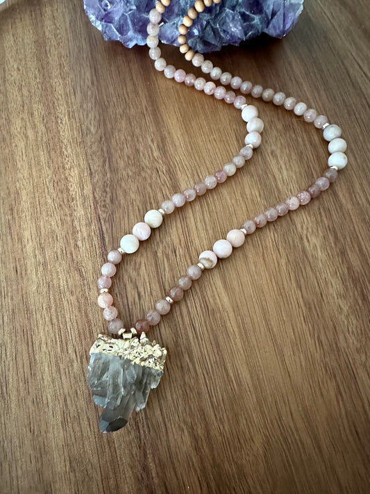 a necklace with pink beads and a smokey quartz pendant on a wooden background with an amethyst stone