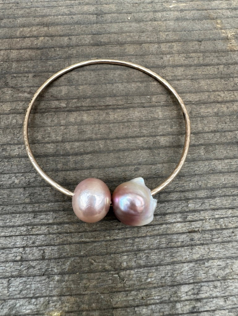 two pearls on a gold wire bracelet on a wooden background