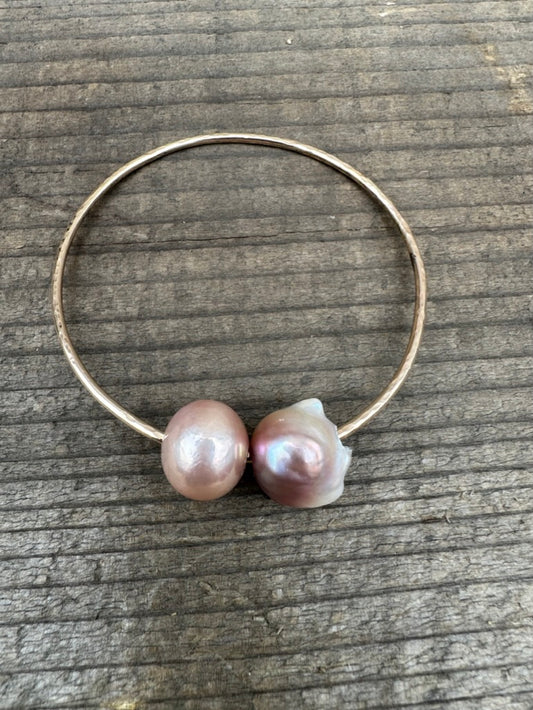 two pearls on a gold wire bracelet on a wooden background