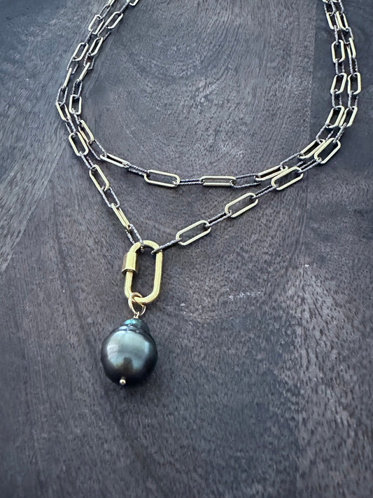 a large Tahitian pear on a gold carabiner on a mixed metal chain of sterling silver and gold on a wooden background. the necklace is double layered .
