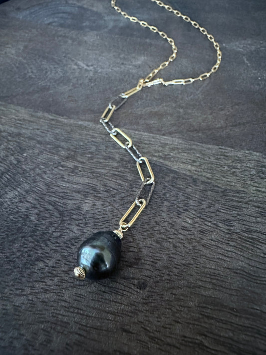 a black pearl on a long 5" mixed gold and silver chain off of a gold paperclip chian on a grey wooden background