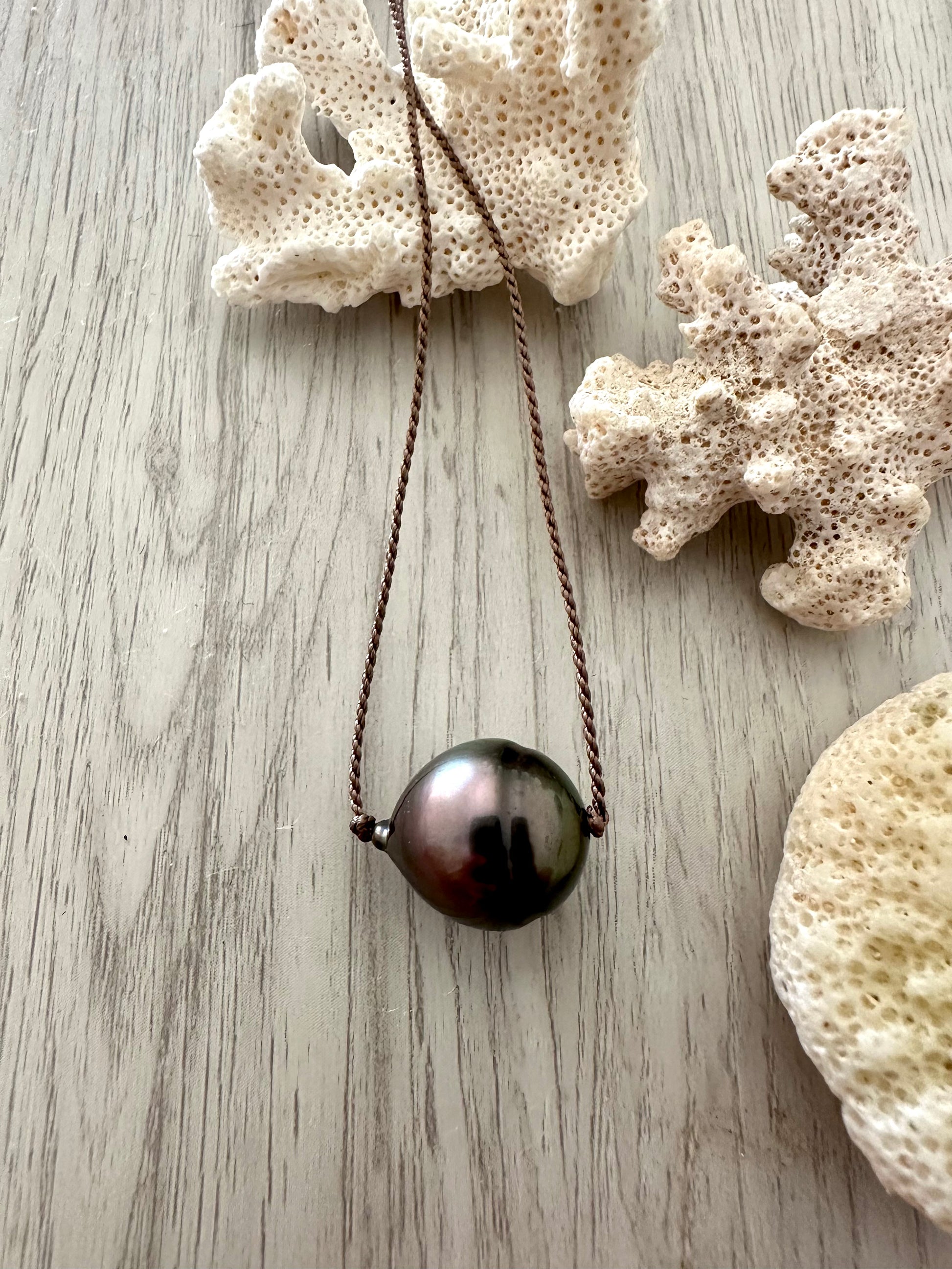 a large black pearl on dark grey cord is laying over white coral on a light grey background
