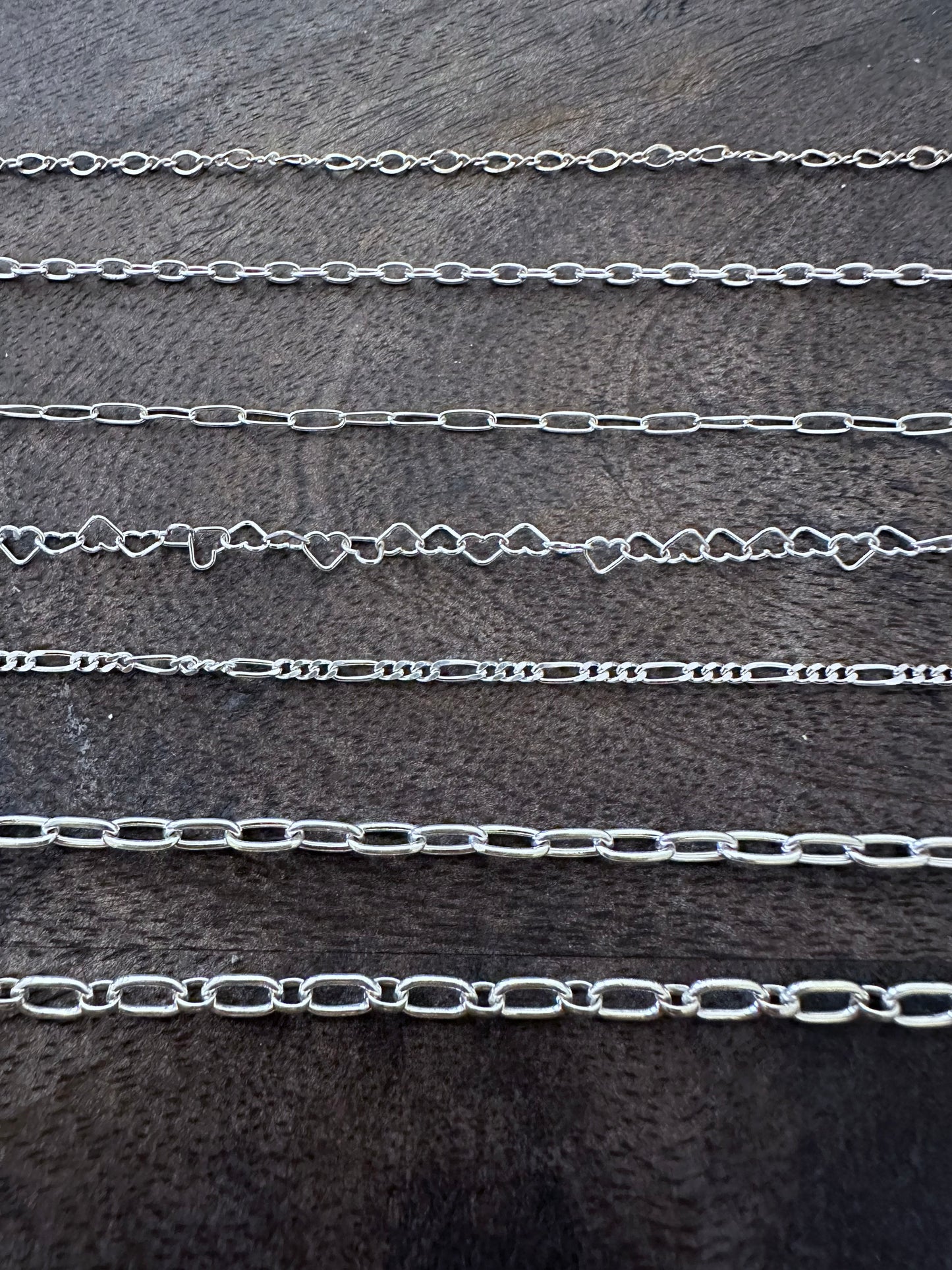 7 sterling silver chains on a wooden background descending in size. 