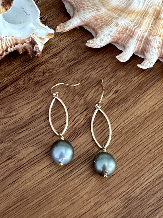 A pair of black pearl earrings dangling off of a marquis shaped drop in gold on a wooden back ground