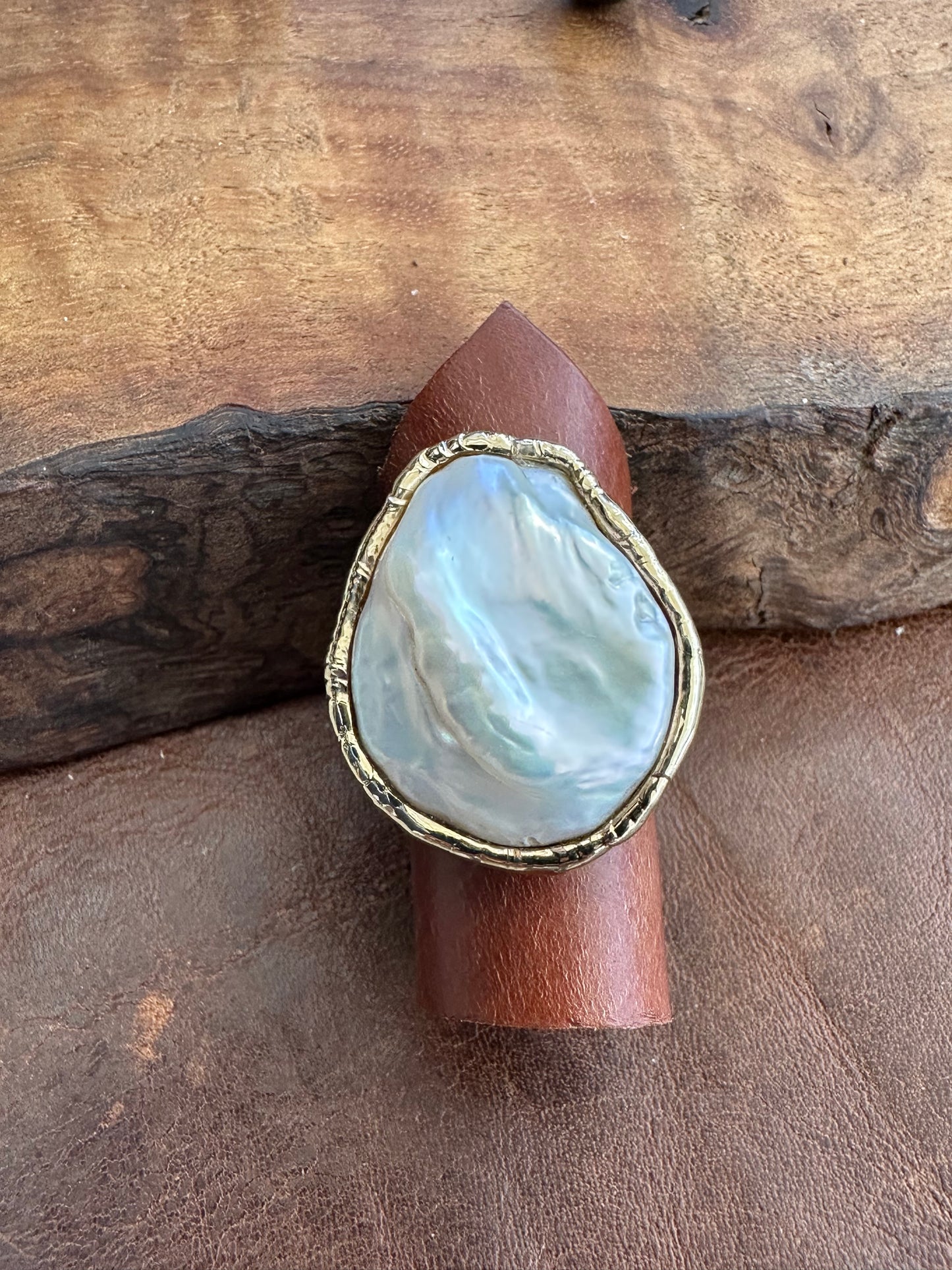a large white cloud shaped ring on a  piece of leather laying on a wooden backdrop