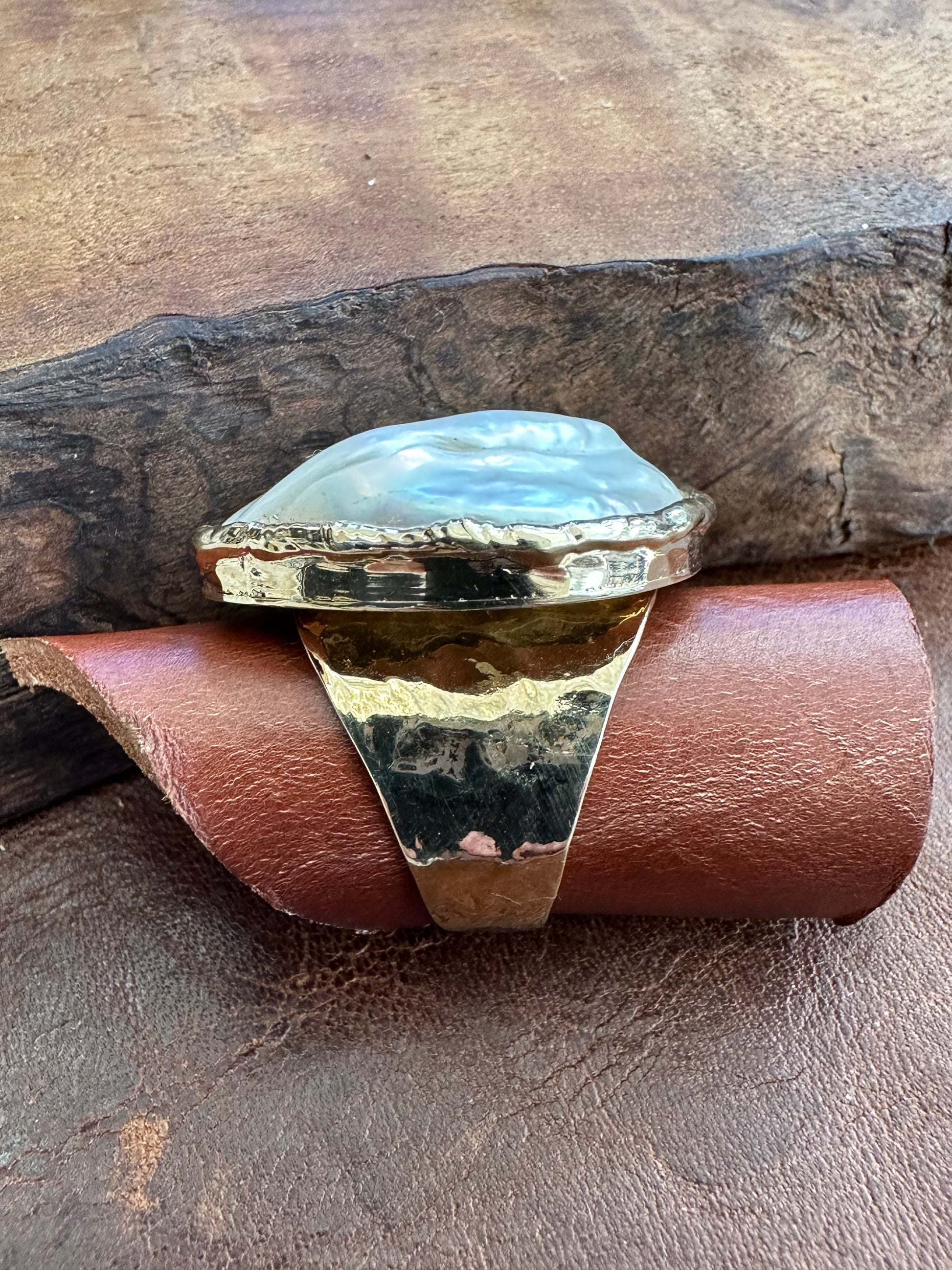 side view of a large white cloud shaped ring on a piece of leather laying on a wooden backdrop