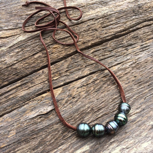 five Tahitian pearls on a dark brown leather cord on a wooden background