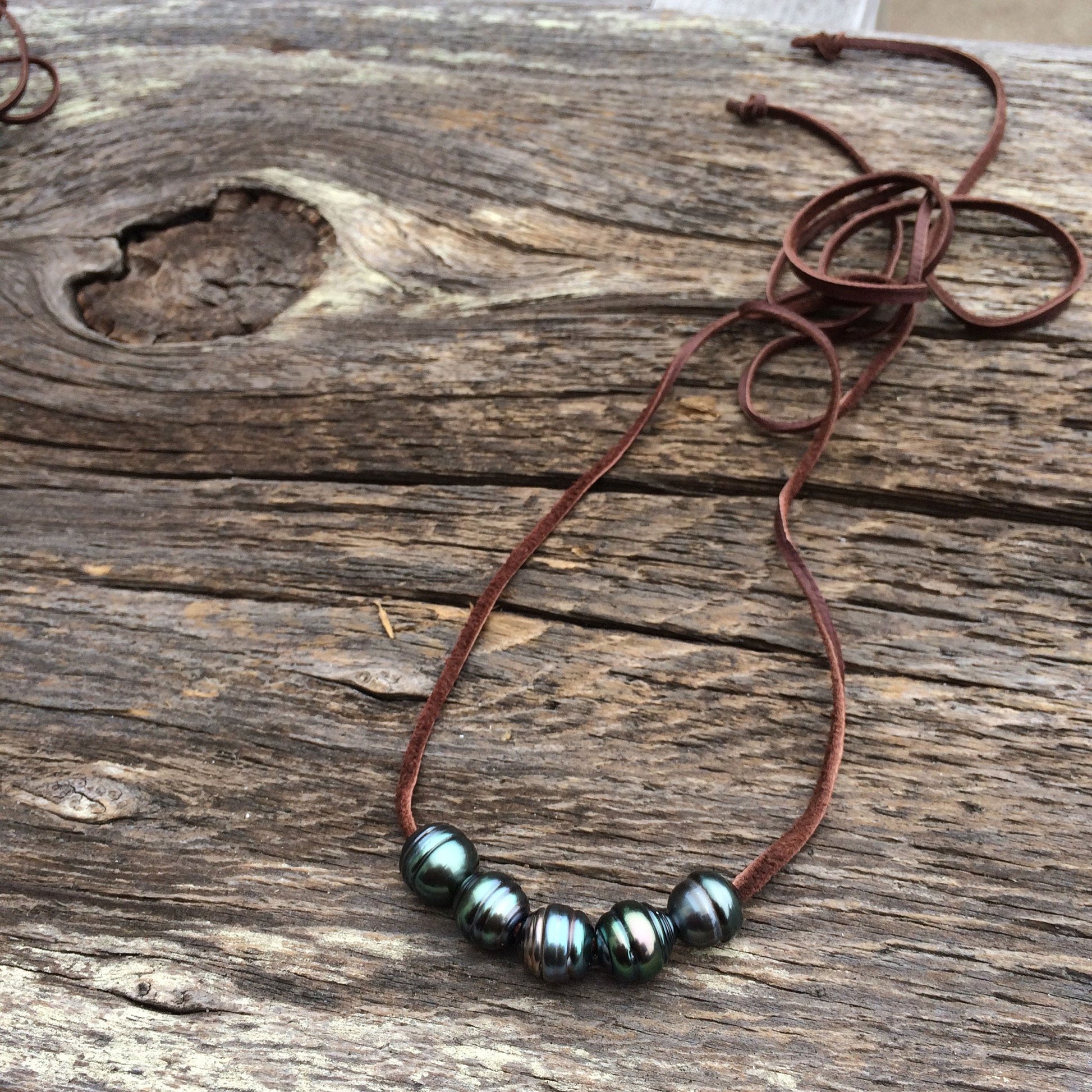 five Tahitian pearls on a dark brown leather cord on a wooden background