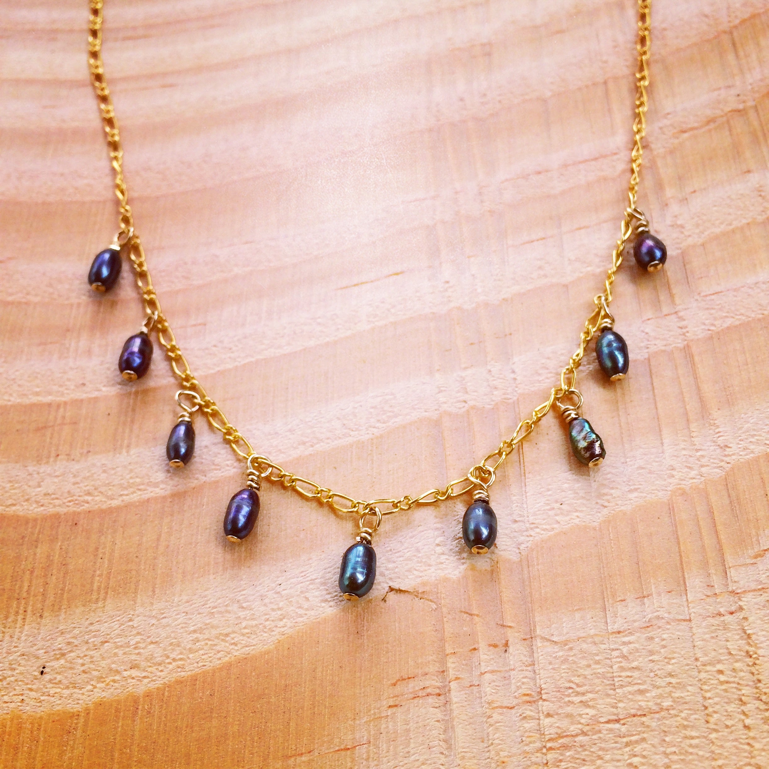 necklace with 9 tiny black pearls spaced 1'4 inch apart dangling on a gold chain on wooden background