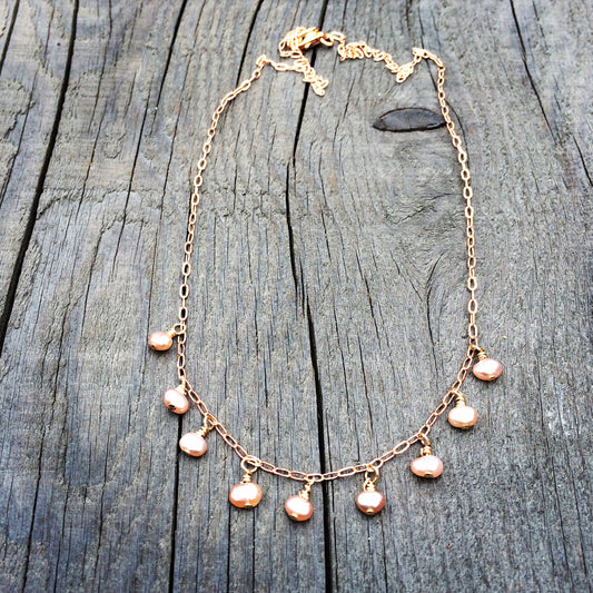necklace with 9 tiny pink pearls spaced 1'4 inch apart dangling on a gold chain on wooden background