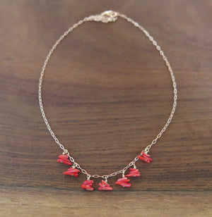 Necklace of 7 drops of little red coral chips dangling spaced apart on a rosegold chain resting on a wooden background