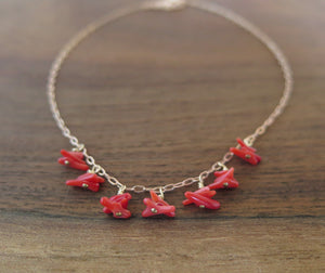 Necklace of 7 drops of little red coral chips dangling spaced apart on a rosegold chain resting on a wooden background