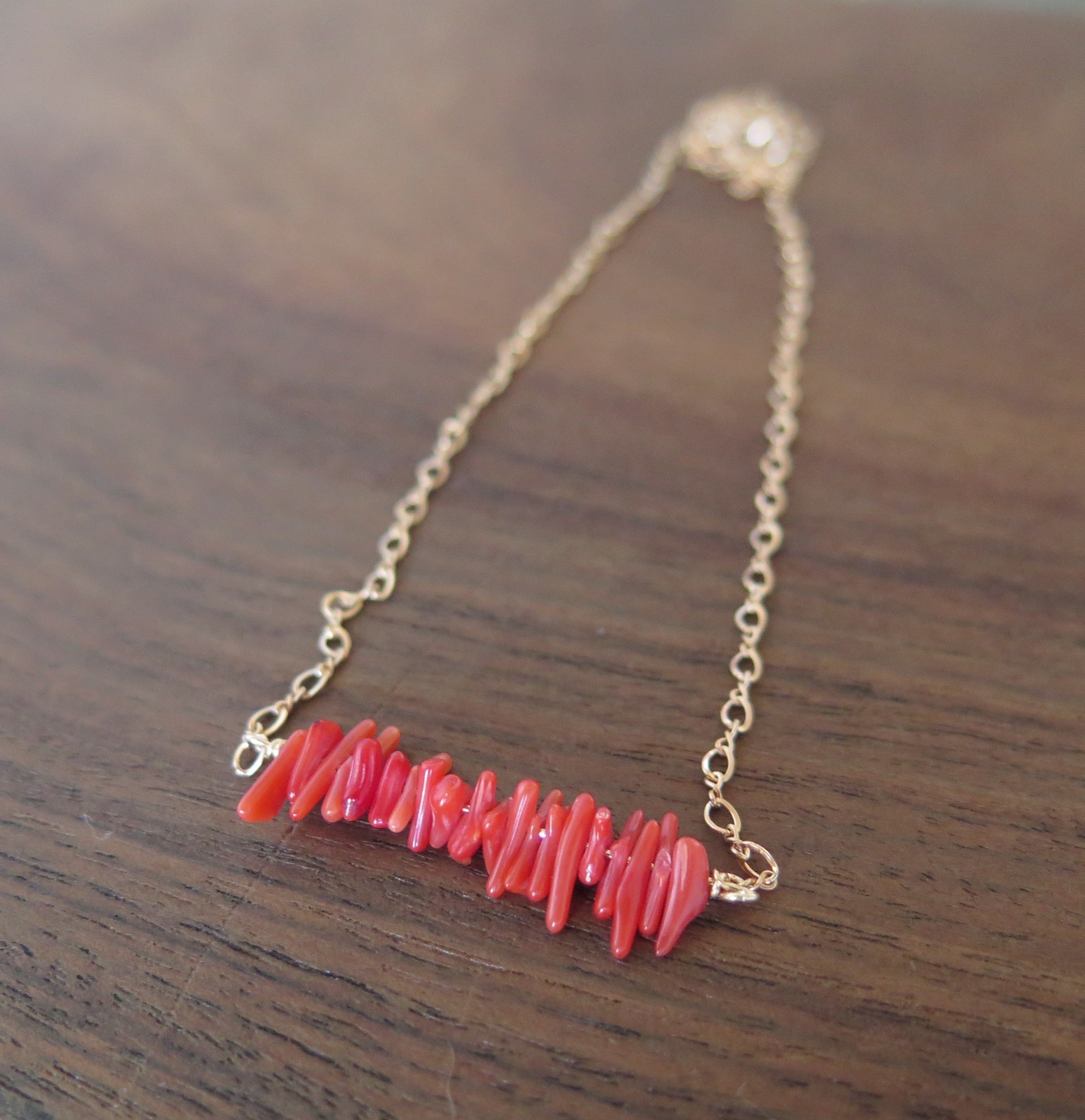 red coral in a row on a rose gold chain on a wooden background
