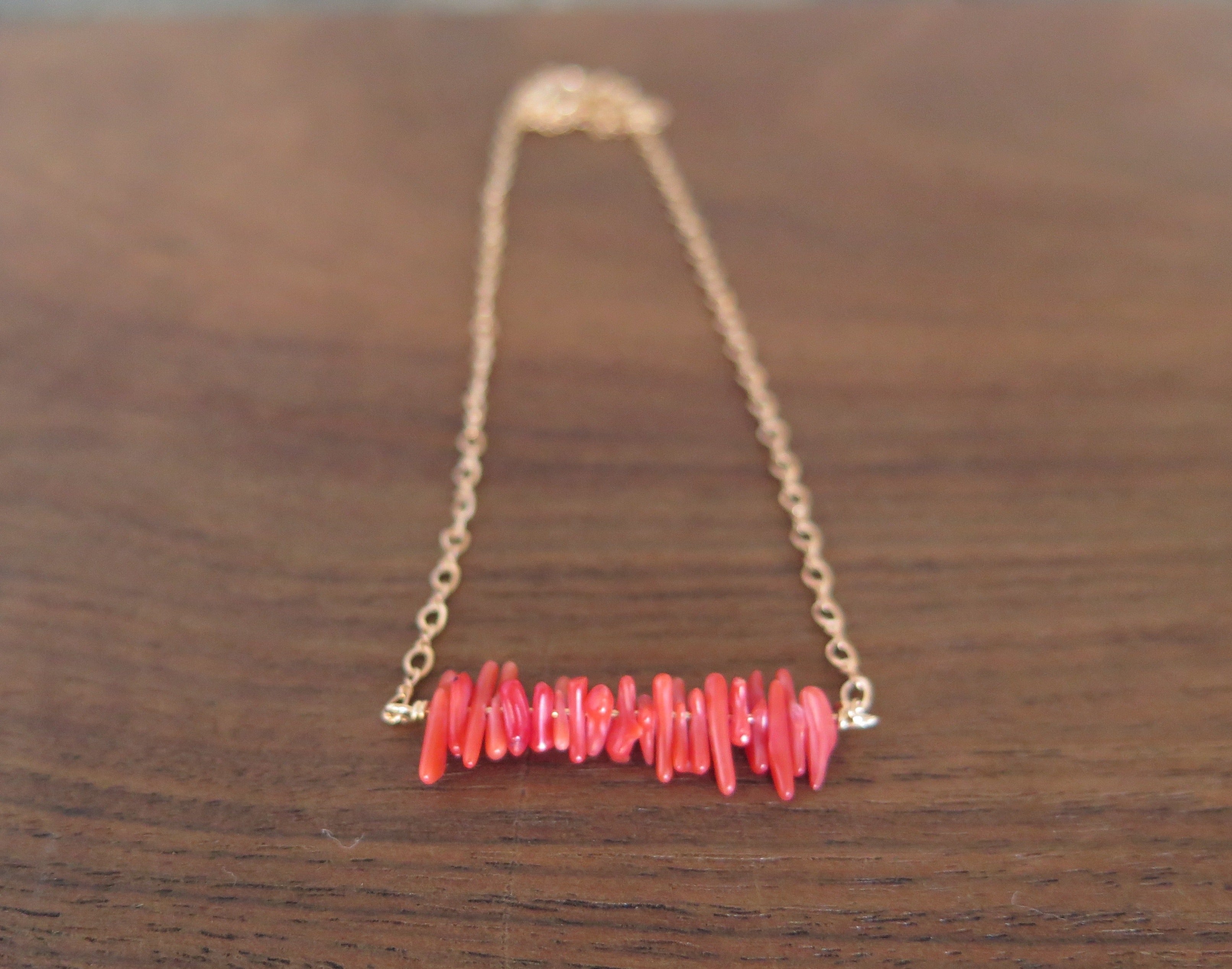 red coral in a row on a rose gold chain on a wooden background