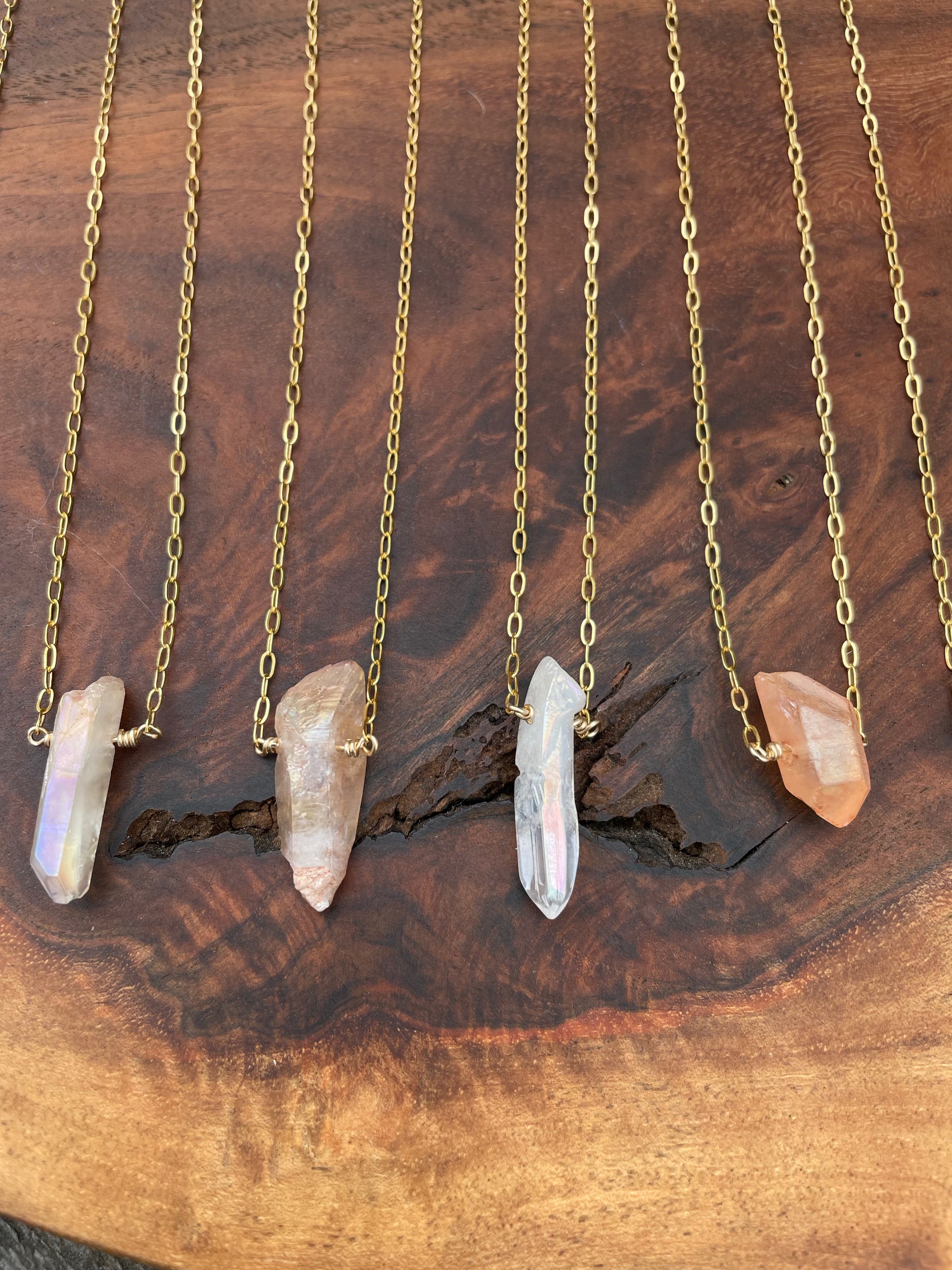 Four rough crystal necklaces in a row on a wooden background. white, pinky and orange in color.