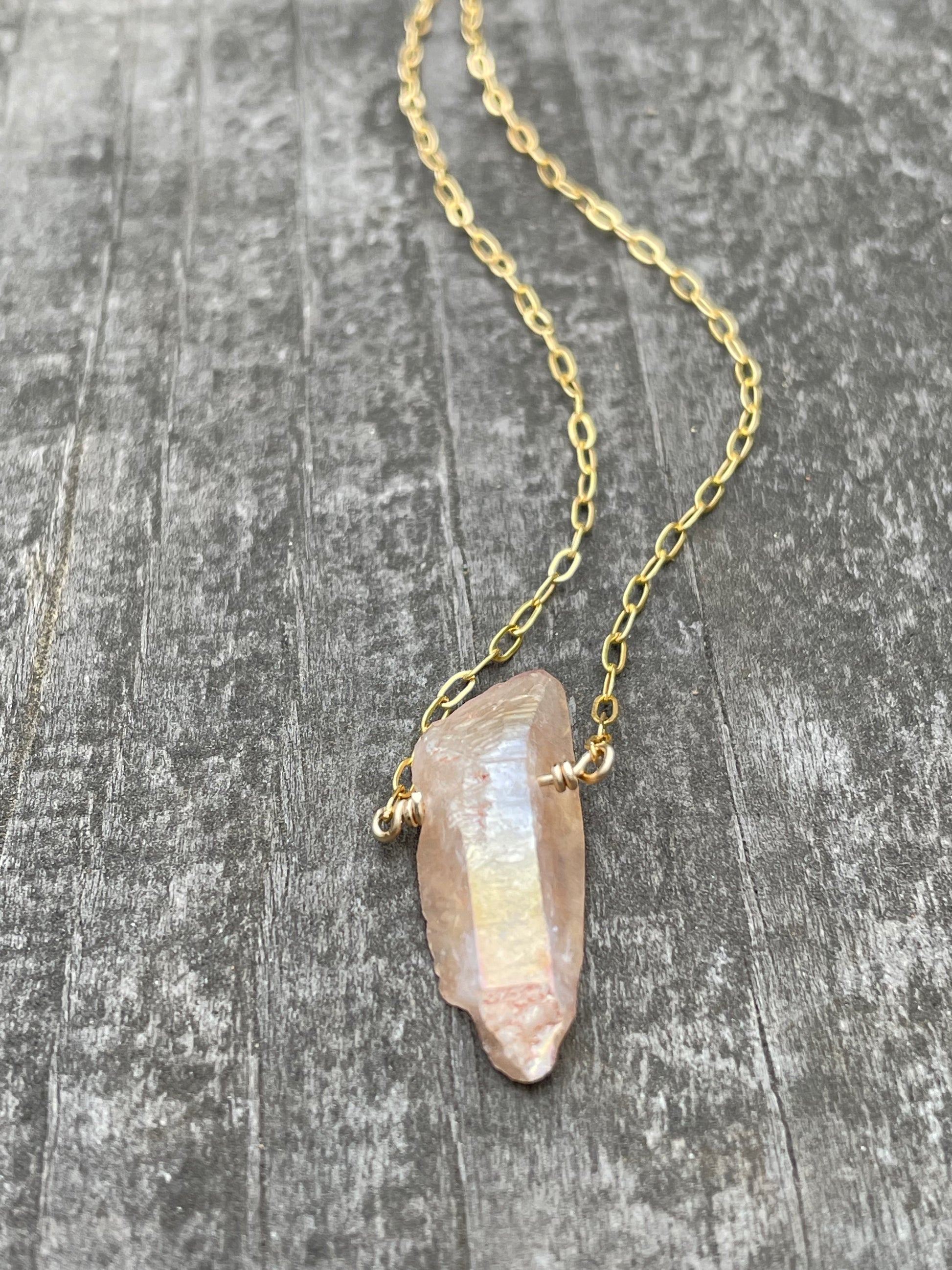 Peach sheen on a quartz crystal wire wrapped onto a gold chain on a wooden background.