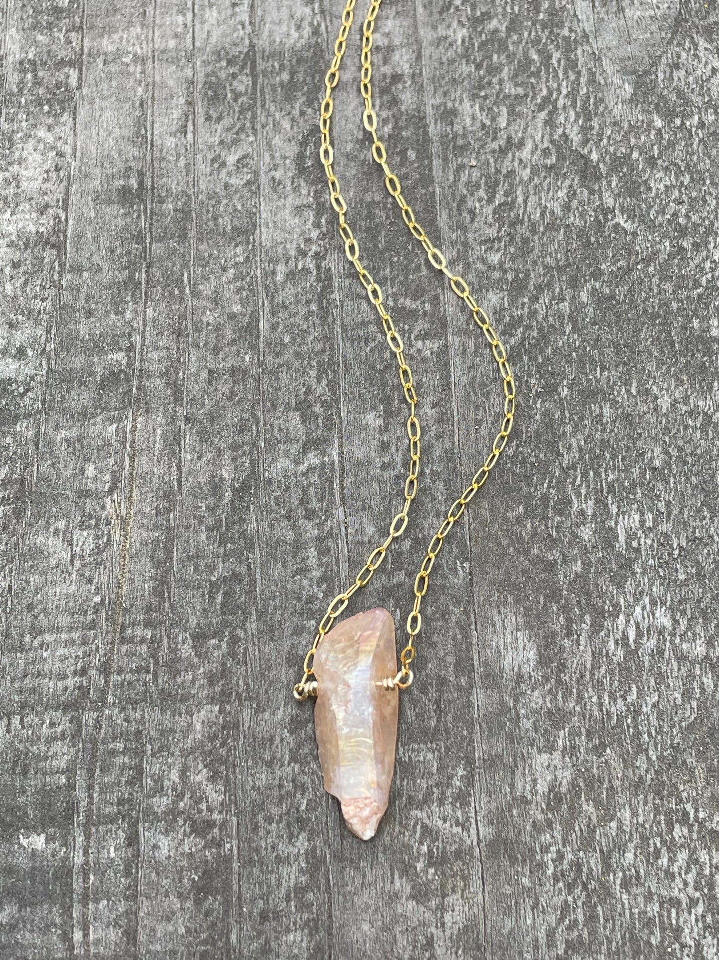 Peach sheen on a quartz crystal wire wrapped onto a gold chain on a wooden background.