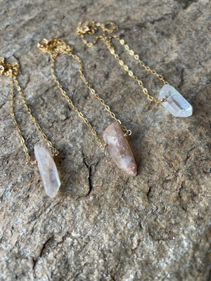 Three  rough crystal necklaces on a stone background. Two white ones and a pink one in the center.