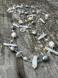 a long silk knotted pearl necklace with white and grey pearls on a wooden backdrop