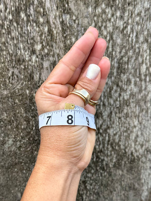 A woman's hand with thumb and pinky touching with a measuring tape wrapped around her palm showing a measurement held up against a wooden back ground.