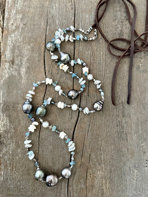 long strand of Tahitian pearls, aquamarine, mini puka shells and grey seed beads  with a dark brown leather tie on a grey wooden background