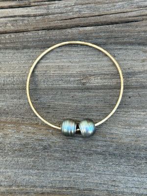 Two black baroque Tahitian pearls on a gold bangle resting on a wooden background