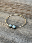 Two black baroque Tahitian pearls on a gold bangle resting on a wooden background