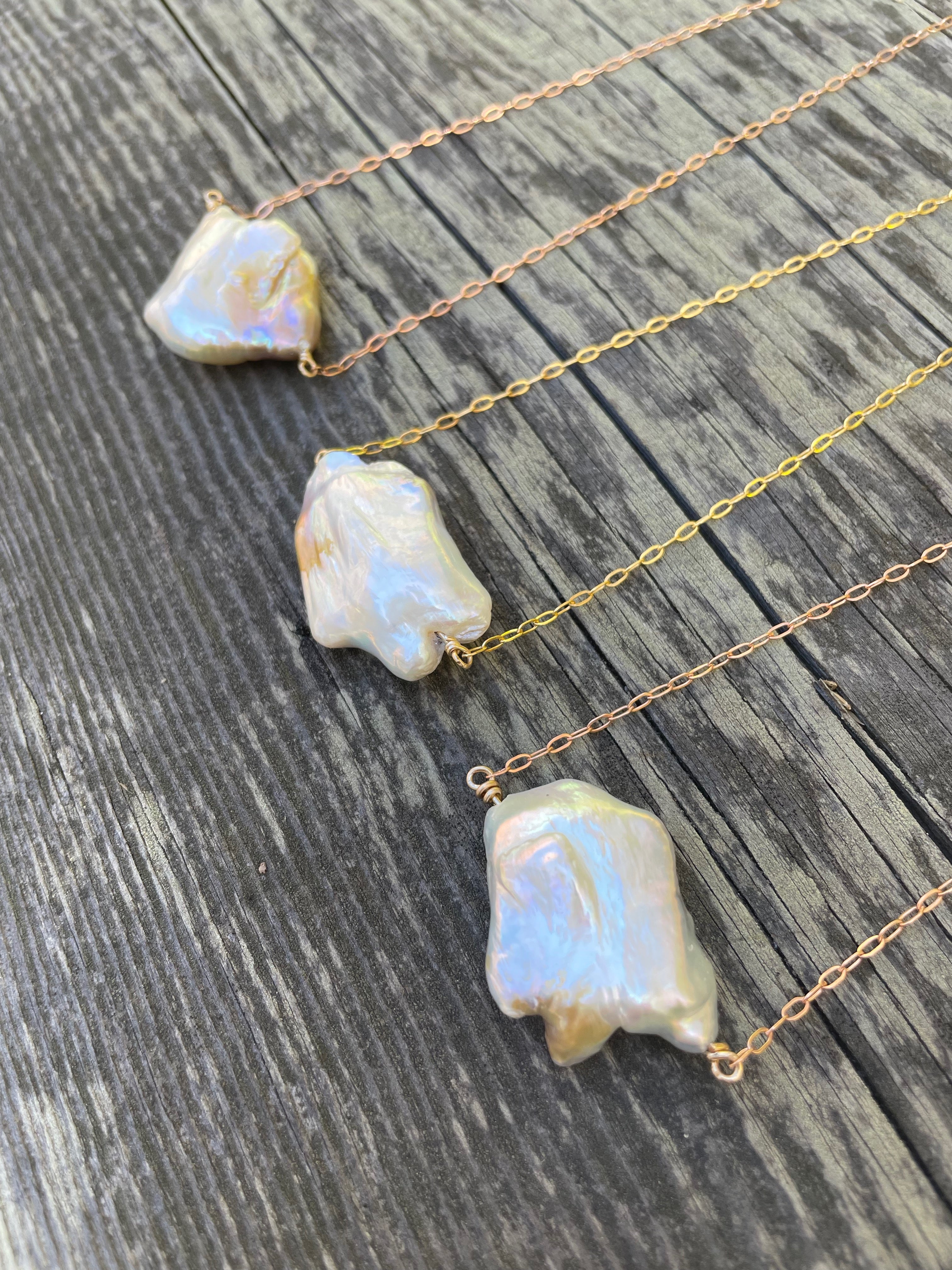 Three large white cloud shaped pearls on gold chains on a wood background
