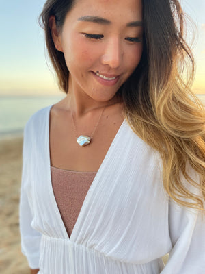 Pretty asian woman on a beach with a white dress on wearing a large white cloud shaped pearl necklace