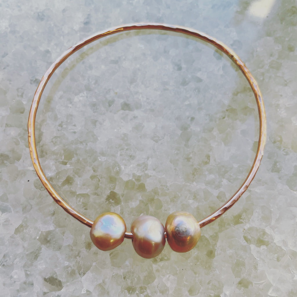 on a crystal background lays a rose gold bangle with three pink pearls.