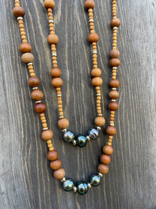 Two necklaces of Round wooden beads in two different sizes with gold beads and three blueish grey dark Tahitian pearls on a wooden background 
