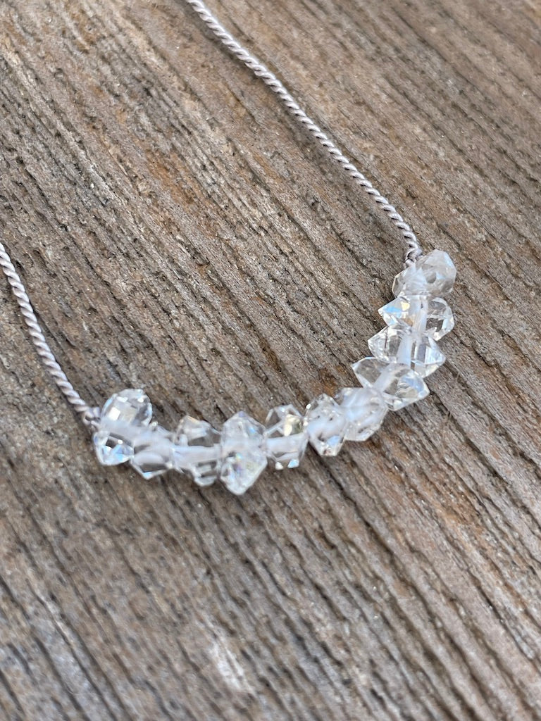 A row of herkimer Diamond stones on a grey silk necklace on a wooden background