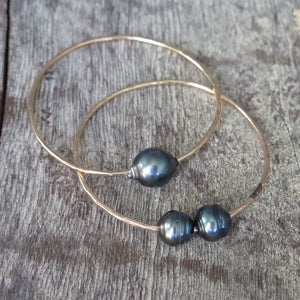 Two gold bangles one with a single Tahtian pearl and one with two Tahitian pearls.