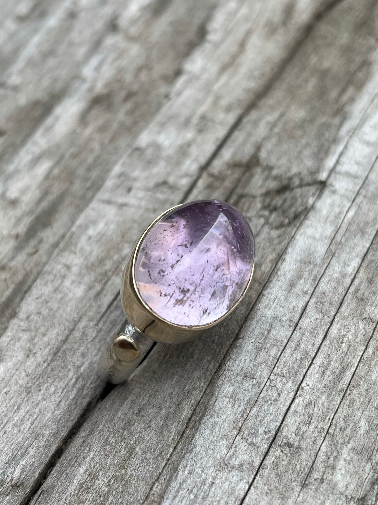 a large purple domes ring with a gold band around it and gold round accent on a silver band sits in some grey wood.