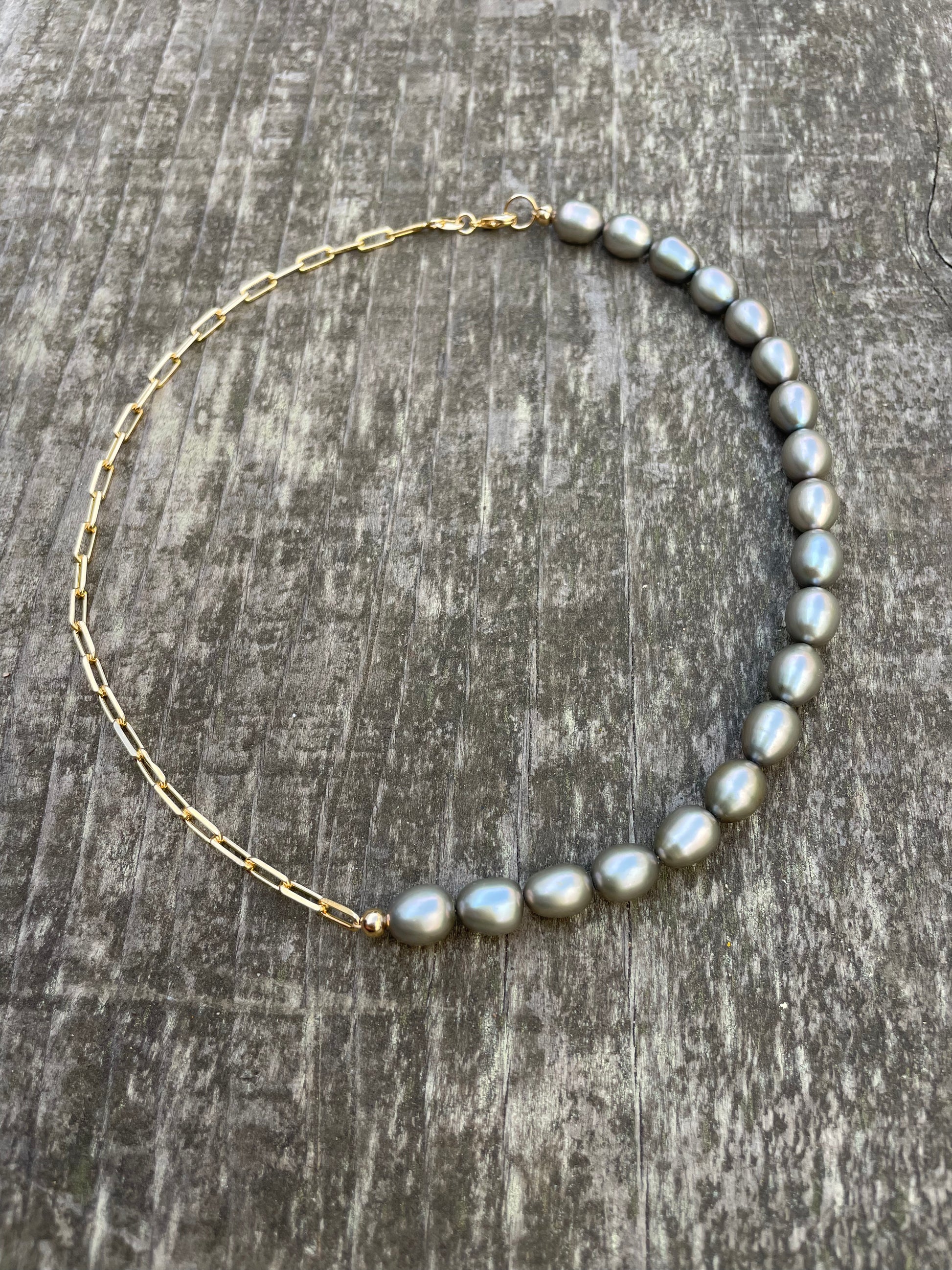 A choker necklace with half grey freshwater pearls and half gold chain on a wooden background 