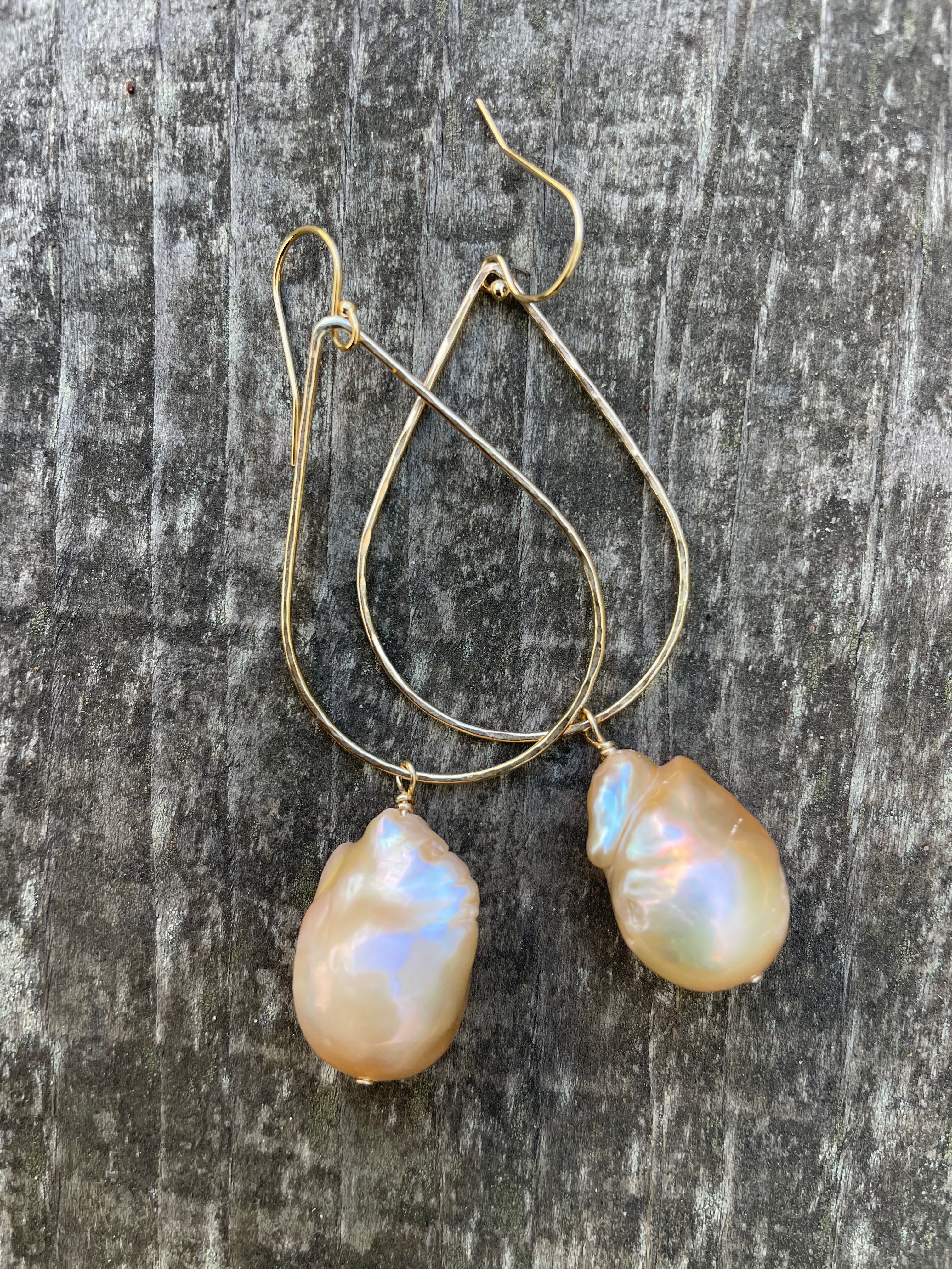 Large pink baroque fireball pearls hanging off of a teardrop shaped gold wire with ear wires on a wooden background.