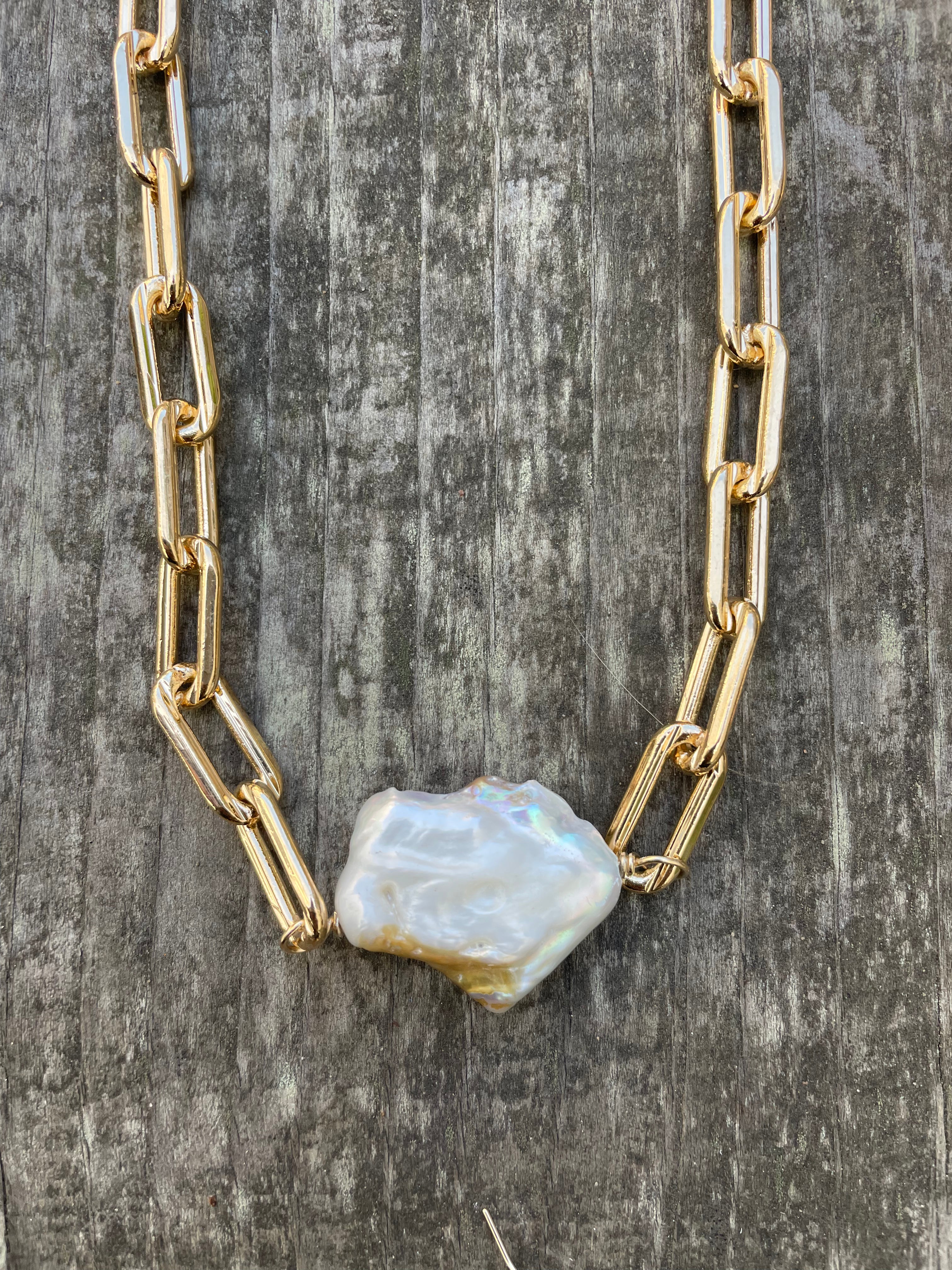 Extra large gold linked chain with a large white cloud shaped pearl on a wooden background