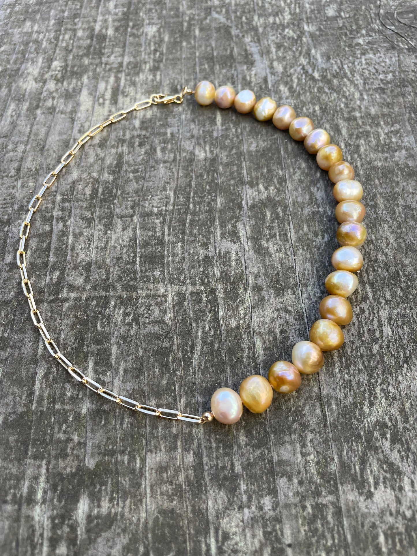 A choker necklace with half gold chain and half golden pearls on a wooden background