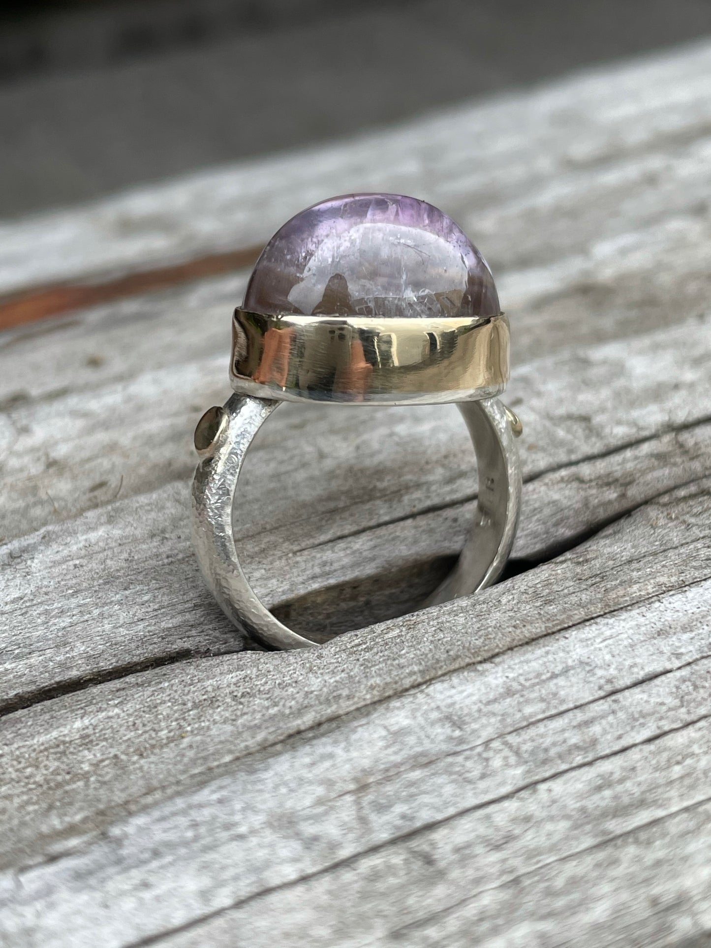 a side view of this purple domed ring with a gold band and a silver shank sits in a piece of grey drift wood