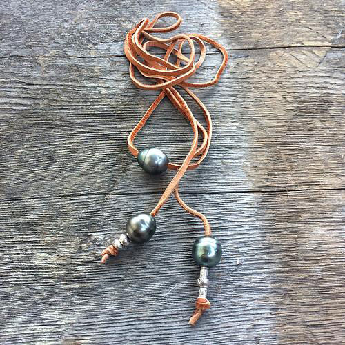 three black pearls on a suede cord with silve beads is coiled up on a wooden background