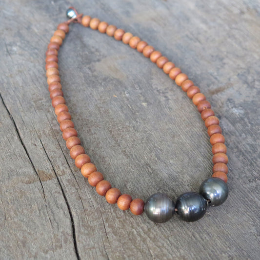 a neckalce with wooden beads and three large black pearls on a grey wooden background
